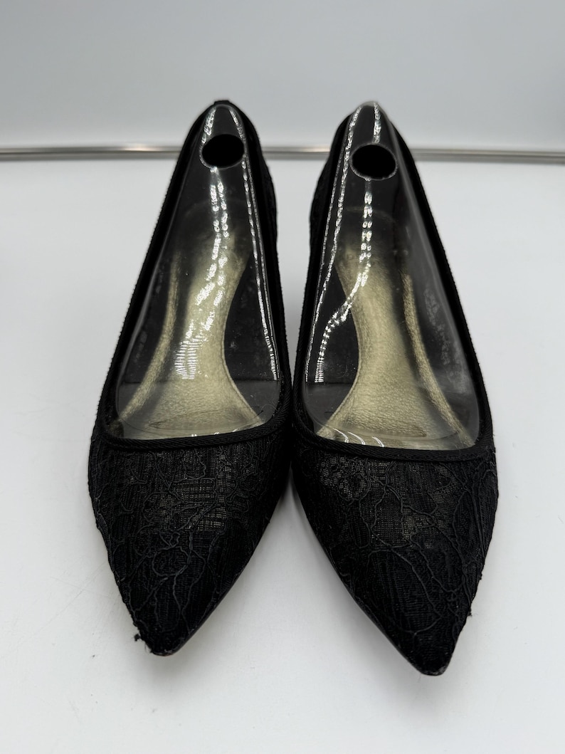 K&ouml;nnte beinhalten: Ein Paar schwarze Pumps mit spitzer Zehenpartie. Die Schuhe haben eine zarte Spitzenauflage auf der Zehenbox und den Seiten. Die Abs&auml;tze sind von moderater H&ouml;he, und die Innensohle ist durch ein transparentes Obermaterial aus Kunststoff sichtbar.