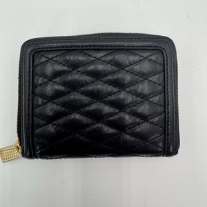 Puede incluir: Cartera de cuero negro acolchado con cremallera y tirador dorados. La cartera tiene un patr&oacute;n de diamantes y forma rectangular. La cremallera recorre tres lados de la cartera.
