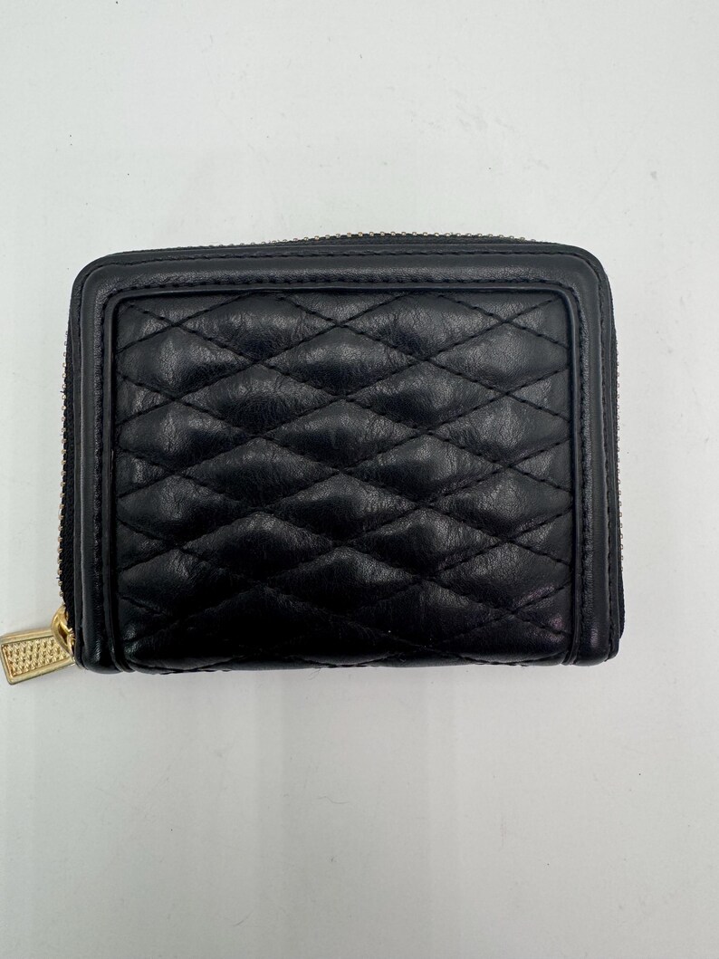 Puede incluir: Cartera de cuero negro acolchado con cremallera y tirador dorados. La cartera tiene un patr&oacute;n de diamantes y forma rectangular. La cremallera recorre tres lados de la cartera.