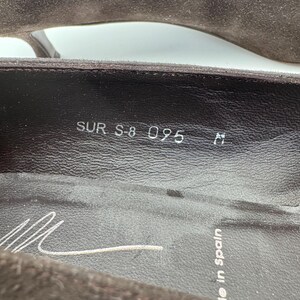 May include: Close-up of a brown suede shoe interior. The shoe's insole displays the text "SUR S-8 095 M" and a signature. The words "Made in Spain" are also visible.