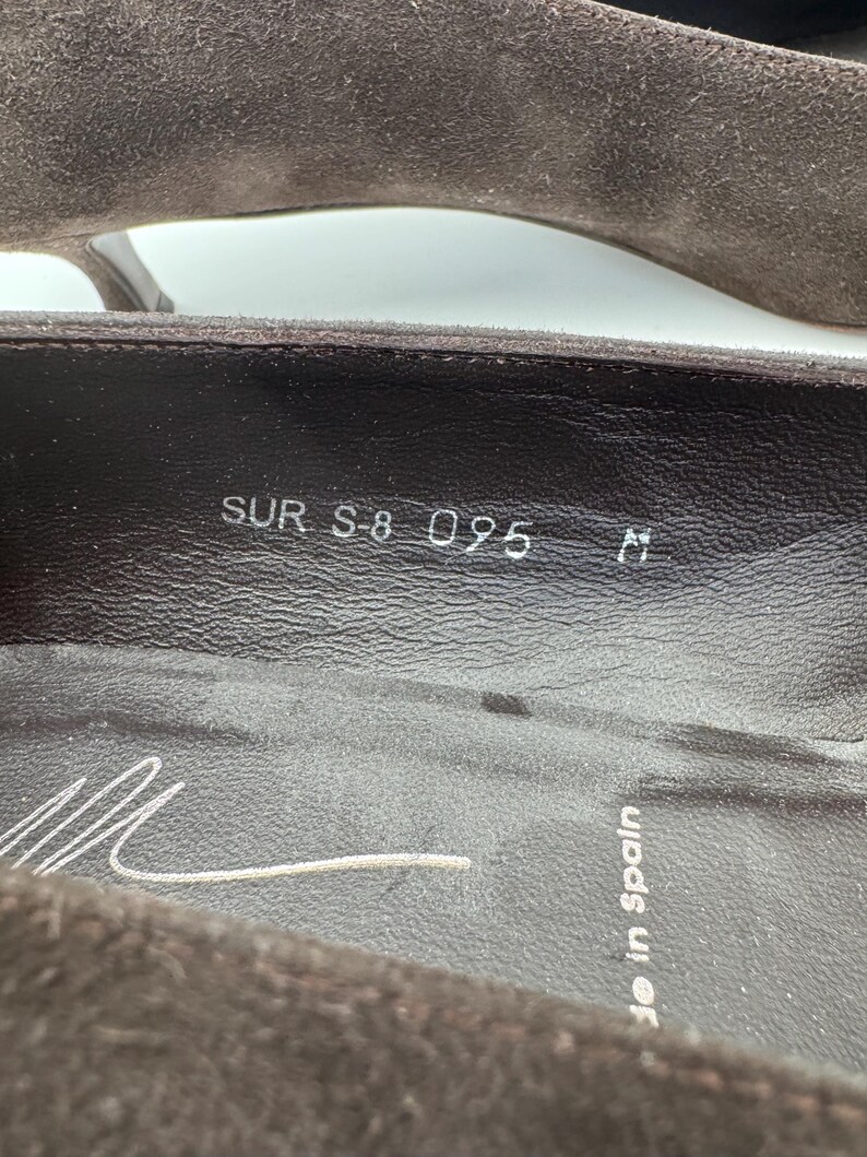 May include: Close-up of a brown suede shoe interior. The shoe's insole displays the text "SUR S-8 095 M" and a signature. The words "Made in Spain" are also visible.