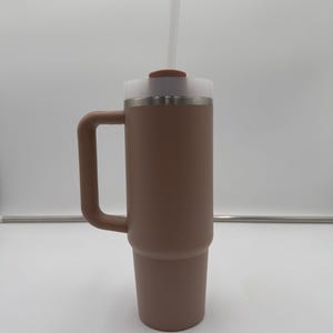 Pu&ograve; includere: Un bicchiere termico marrone con manico, coperchio in plastica trasparente e cannuccia trasparente. Il bicchiere &egrave; cilindrico con una base leggermente affusolata. Il coperchio ha un piccolo pezzo circolare marrone sopra.