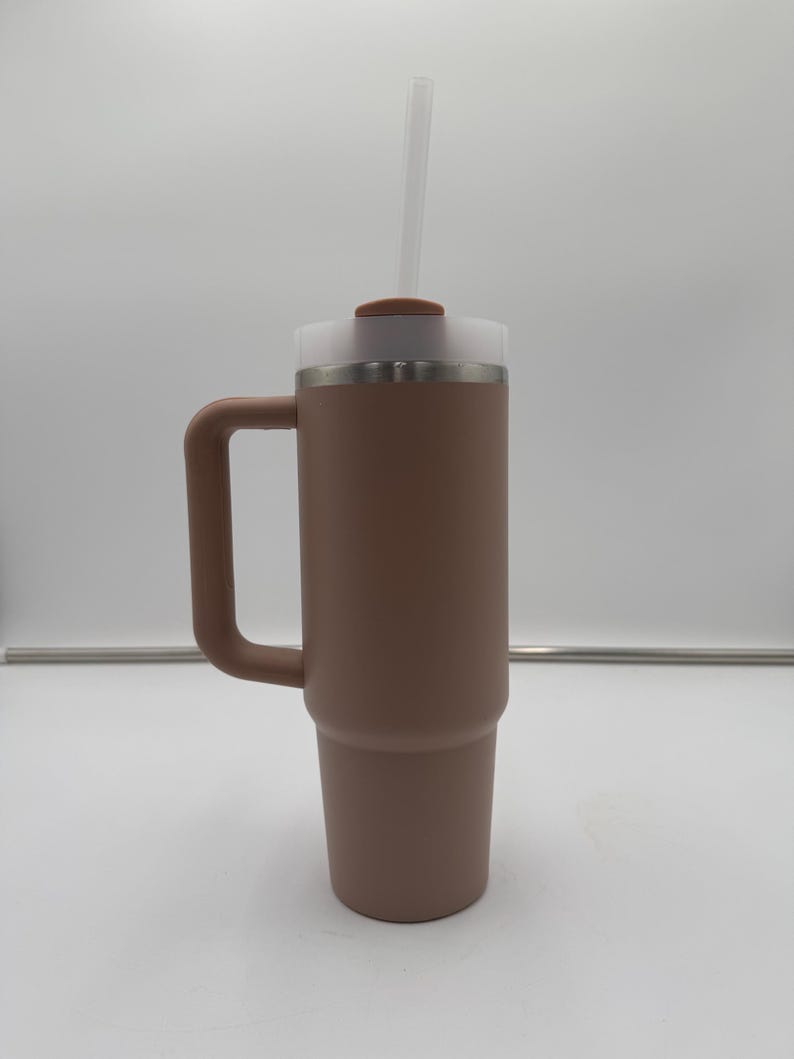 Pu&ograve; includere: Un bicchiere termico marrone con manico, coperchio in plastica trasparente e cannuccia trasparente. Il bicchiere &egrave; cilindrico con una base leggermente affusolata. Il coperchio ha un piccolo pezzo circolare marrone sopra.
