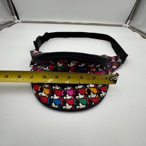 May include: A colorful fanny pack featuring a repeating grid pattern of Mickey Mouse heads in red, blue, yellow, and green squares. A yellow measuring tape is placed across the front, showing a width of approximately 8 inches for the bag.