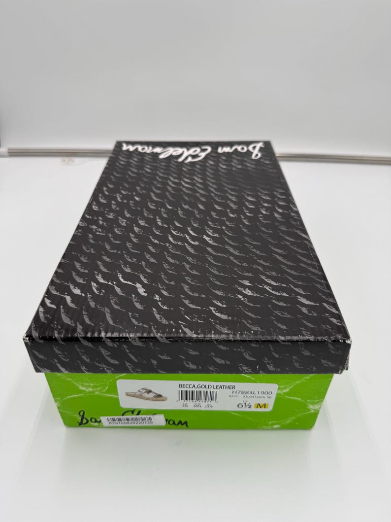 May include: A rectangular shoe box with a black lid featuring a textured pattern and the brand name "Sam Edelman." The box has a green base with product information, including "BECCA, GOLD LEATHER" and size 6 1/2 M.