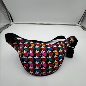 May include: A waist bag featuring a repeating grid pattern of Mickey Mouse silhouettes in black against colorful squares of red, yellow, green, blue, and pink. The bag includes a black adjustable strap with a black plastic side-release buckle.