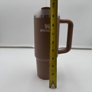 Pu&ograve; includere: Un bicchiere Stanley marrone con manico, cannuccia e coperchio. Il bicchiere &egrave; alto circa 25 cm. Il logo Stanley &egrave; visibile sul davanti. Progettato per mantenere le bevande fredde o calde.
