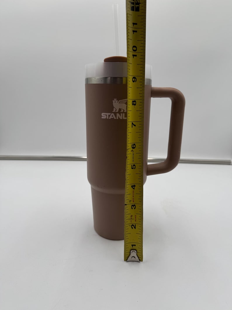 Pu&ograve; includere: Un bicchiere Stanley marrone con manico, cannuccia e coperchio. Il bicchiere &egrave; alto circa 25 cm. Il logo Stanley &egrave; visibile sul davanti. Progettato per mantenere le bevande fredde o calde.