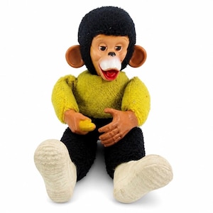 May include: A plush monkey toy with a black fuzzy head, a yellow fuzzy long-sleeved shirt, and black fuzzy pants. The monkey has a tan plastic face with large ears, a white mouth area, and a red interior mouth. It holds a small yellow banana.