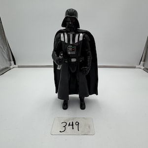 May include: A black Darth Vader action figure with a black cape, helmet, and armor. The figure is holding a silver lightsaber. A silver tag with the number 349 is at the base of the figure.