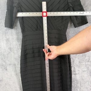 K&ouml;nnte beinhalten: Schwarzes knielanges Kleid mit strukturiertem, geschichtetem Design. Das Kleid hat kurze &Auml;rmel und einen V-Ausschnitt. Das Kleid misst ca. 46 cm &uuml;ber der Brust und 97 cm in der L&auml;nge.