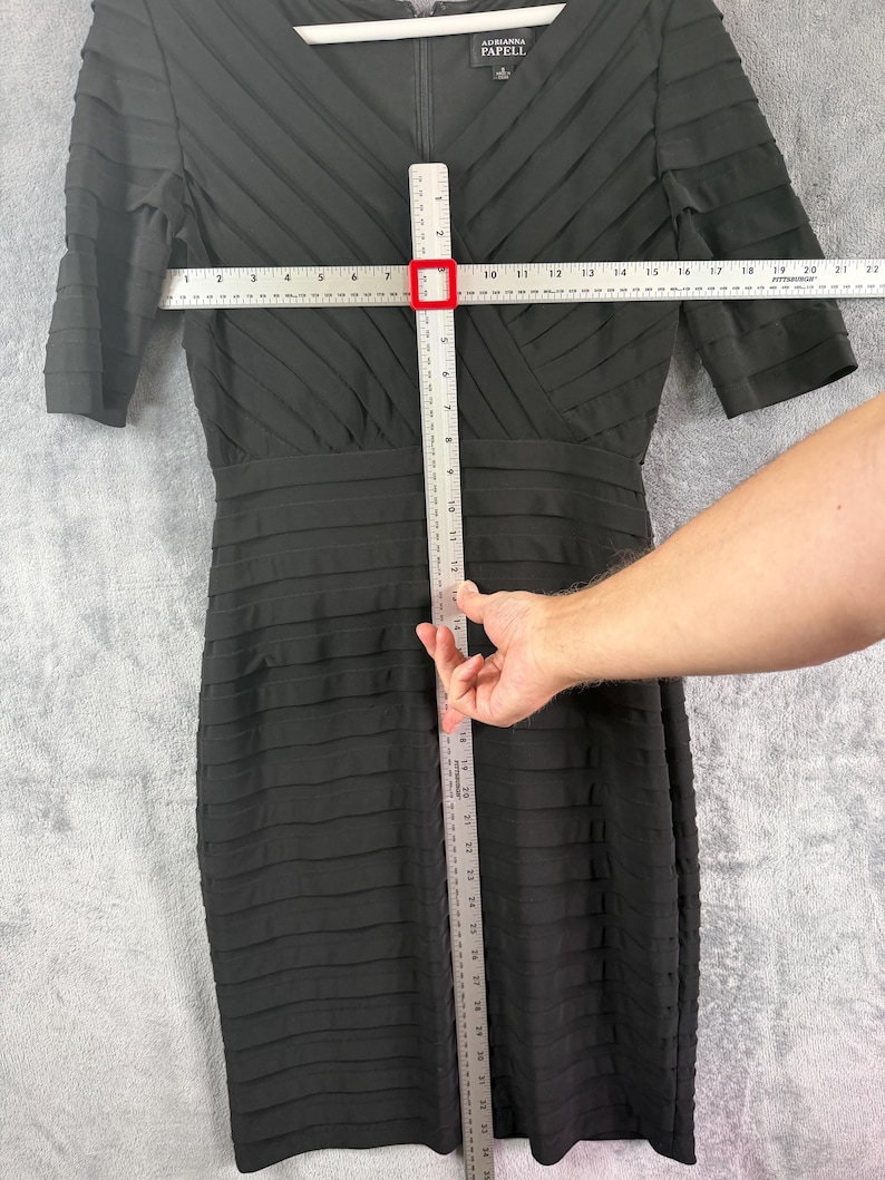 K&ouml;nnte beinhalten: Schwarzes knielanges Kleid mit strukturiertem, geschichtetem Design. Das Kleid hat kurze &Auml;rmel und einen V-Ausschnitt. Das Kleid misst ca. 46 cm &uuml;ber der Brust und 97 cm in der L&auml;nge.