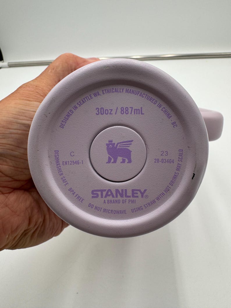 Op de afbeelding: De bodem van een lichtpaarse Stanley-beker. De bodem van de beker heeft de tekst "30oz / 887mL". De tekst "Designed in Seattle WA, Ethically Manufactured in China - BC" is ook zichtbaar.