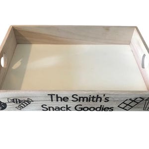May include: A wooden tray with the text "The Smith's Snack Goodies" printed on the front. The tray is decorated with images of a doughnut, sweets, a chocolate bar, and popcorn.