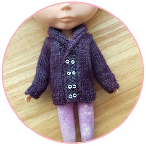 Op de afbeelding: Een paarse gebreide cardigan met een shawlkraag en knoopsluiting. De cardigan heeft een getextureerd breipatroon en wordt gedragen door een pop.