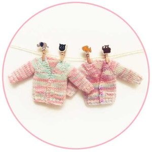 May include: Two pink and white striped knitted cardigans hanging on a clothesline with animal-shaped clothespins.