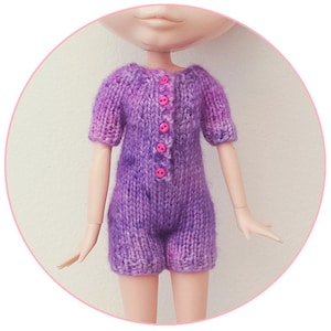 May include: Purple knitted doll romper with pink buttons. The romper has short sleeves and a button-up front.