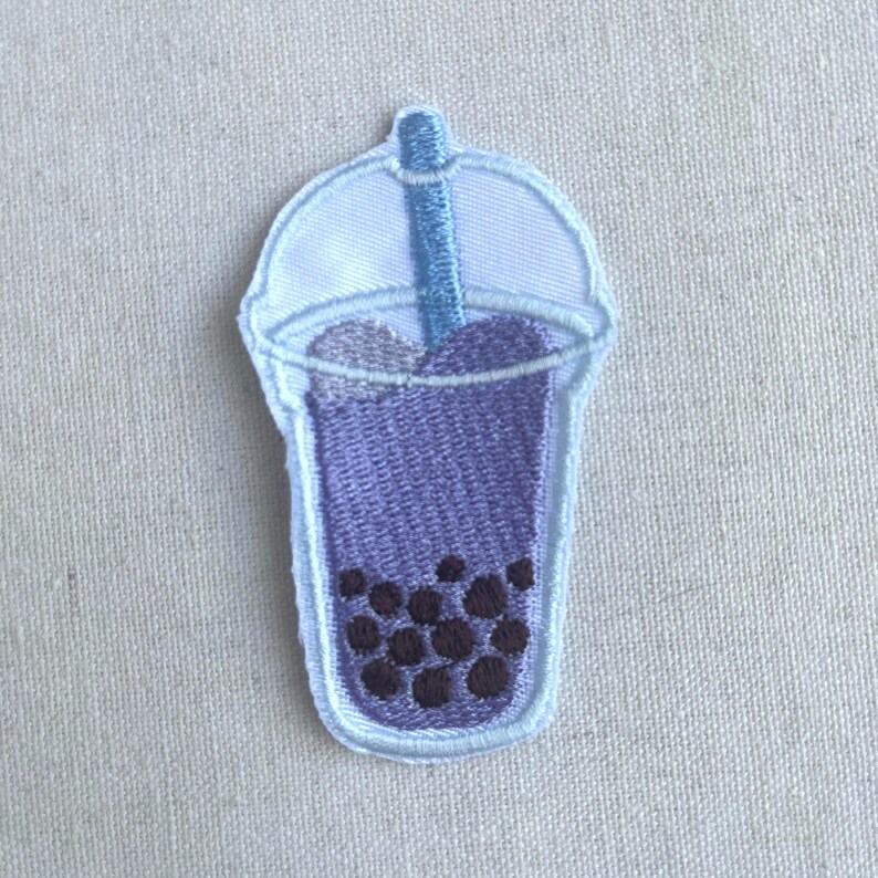 May include: Purple embroidered iron-on patch of a boba tea cup with a blue straw and black boba pearls.