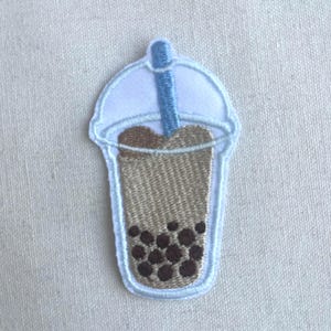 May include: Embroidered iron-on patch of a brown bubble tea with a blue straw and a white lid.