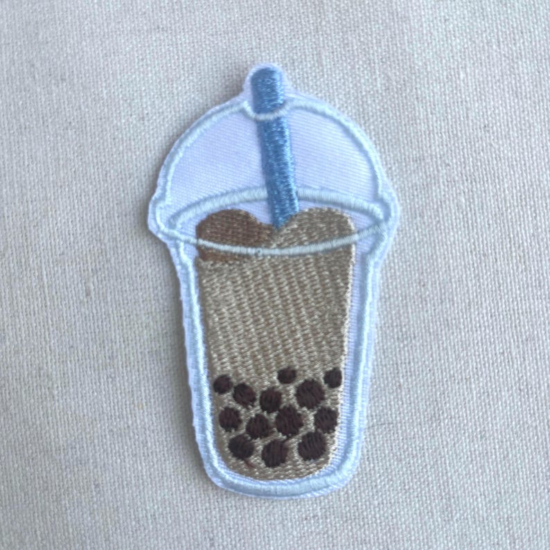 May include: Embroidered iron-on patch of a brown bubble tea with a blue straw and a white lid.