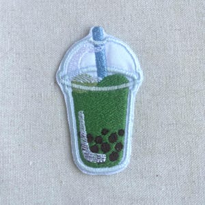 May include: An embroidered patch of a green bubble tea with a white straw and a white lid. The bubble tea has brown tapioca pearls.