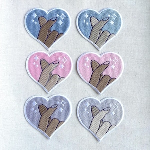 May include: Six heart-shaped embroidered patches with pink and blue backgrounds. Each patch features a pair of hands making a pinky promise with white stars and glitter accents.