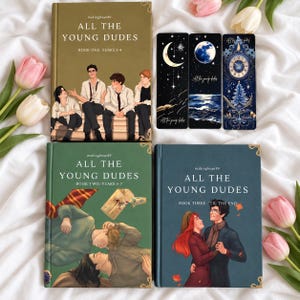 May include: Three hardcover books titled All The Young Dudes by mskingbean89, featuring illustrated covers with characters, and three vertical bookmarks with celestial, moon, and clock designs, arranged on a white fabric surface.