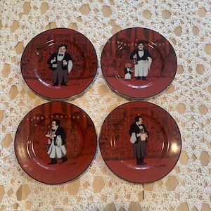 May include: Set of four red decorative plates featuring illustrations of waiters in a restaurant setting. Each plate has a black rim and a unique waiter illustration. The plates are on a cream-colored lace tablecloth.