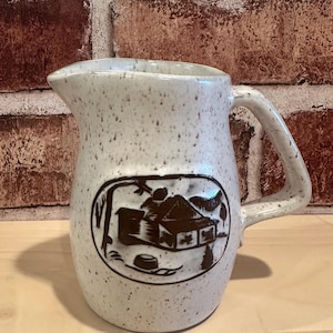 May include: A set of three ceramic mugs with a speckled, matte finish. The mugs are in shades of cream, light gray, and dark gray. Each mug has a simple, minimalist design and a rounded handle. The mugs are stacked on top of each other.