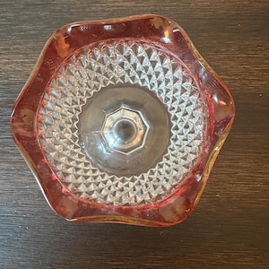 May include: A vintage, clear glass bowl with a ruby red rim and a textured, diamond-patterned interior. The bowl has a hexagonal base and a scalloped edge. The glass has a slight amber hue.