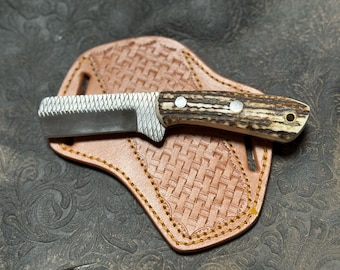 Puede incluir: Un pequeño cuchillo con mango marrón, hoja dentada y funda de cuero. La funda tiene un patrón tejido y está cosida con hilo marrón.