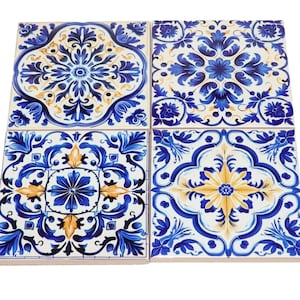 May include: A set of four square ceramic tiles arranged in a grid, each featuring a distinct blue, white, and yellow floral and geometric pattern. The tiles display intricate symmetrical designs with deep blue foliage and golden yellow accents.