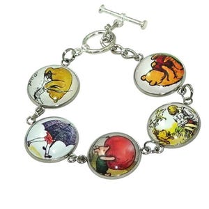 May include: A silver-toned toggle clasp bracelet featuring five circular charms. Each charm displays a colorful illustration of Winnie the Pooh characters, including Pooh Bear, Piglet, and Eeyore, set under a clear, rounded glass dome finish.