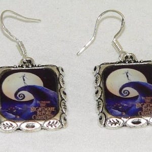May include: Silver tone earrings with a square shaped charm featuring a colorful image of Jack Skellington from the movie "The Nightmare Before Christmas". The charm has a silver tone border with an ornate design.