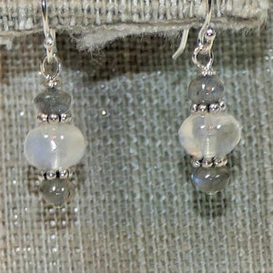 May include: A pair of silver dangle earrings with a white moonstone bead and two gray beads on each earring.
