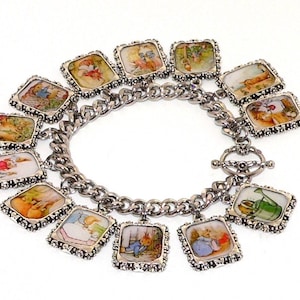 May include: A silver-toned charm bracelet featuring twelve square charms, each displaying a unique colorful illustration of a rabbit character in various scenes. The bracelet is constructed with a thick curb chain and a toggle clasp closure.