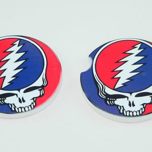 May include: Two round car coasters featuring the Steal Your Face skull logo. The design includes a red and blue circle with a white lightning bolt and skull. The coasters have a small notch for easy removal.