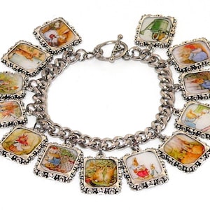 May include: A silver charm bracelet with multiple square charms featuring illustrations from the Peter Rabbit book series. The charms are attached to a silver chain with a lobster clasp.