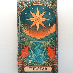 May include: A rectangular, decorative piece featuring a tarot card design. The card depicts a large, eight-pointed star in a teal and orange sky, with two orange pitchers pouring water into a river. The text "THE STAR" is at the bottom.