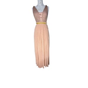 May include: A peach-colored maxi dress with a sleeveless, beaded bodice and a pleated skirt. The dress features a yellow belt at the waist. The dress is displayed on a mannequin.