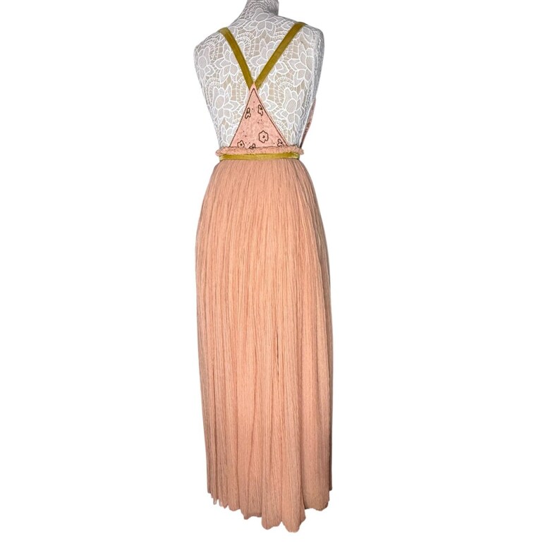 May include: A peach-colored maxi dress with a pleated skirt and a patterned bodice. The bodice features a triangular design with a floral pattern and olive green straps. A gold-colored belt cinches the waist.