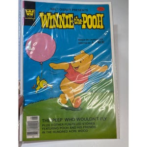 Puede incluir: Un cómic vintage de Winnie the Pooh. La portada presenta una ilustración de dibujos animados de Winnie the Pooh con un globo rosa y un pájaro amarillo sobre un fondo azul. El título dice "Winnie the Pooh" y "The Peep Who Wouldn't Fly."