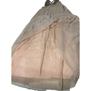 May include: A light peach-colored dress with a pleated design. The dress features a halter neckline with a brown and green patterned top. The skirt of the dress is long and flowing, with a textured appearance.