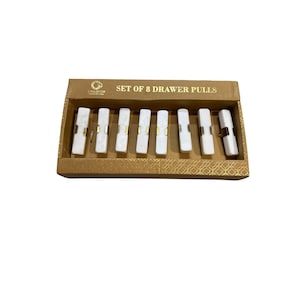 May include: A set of eight white and gold drawer pulls presented in a decorative cardboard box. The drawer pulls are rectangular with gold detailing. The box is labelled "SET OF 8 DRAWER PULLS".