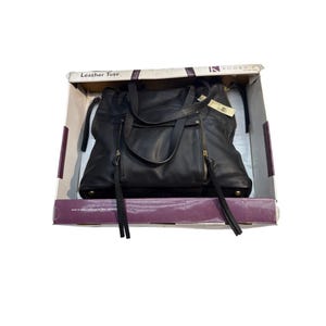 May include: Black leather tote bag with gold-tone zippers and accents, displayed inside a cardboard box. The bag has two handles and a shoulder strap. The box is labeled "Leather Tote" and has the brand name "KOOBA".