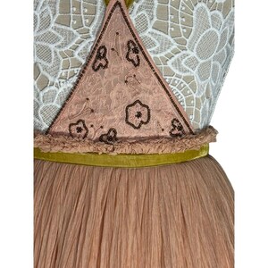 May include: A vintage-style dress featuring a pink tulle skirt and a bodice with a lace overlay. The bodice has a pink triangle with floral embroidery and beaded trim. A green velvet ribbon accents the waist.