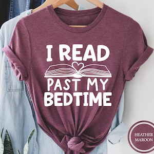 May include: A heather maroon t-shirt with the text "I read past my bedtime" in white. The text is accompanied by a white illustration of an open book with a heart in the center.