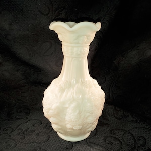 May include: White milk glass vase with a raised floral design. The vase has a wide mouth and a narrow neck.