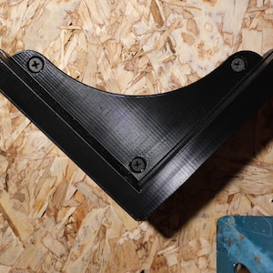 May include: Black plastic corner shelf bracket with three visible screws. The bracket is mounted on a light brown wood surface.