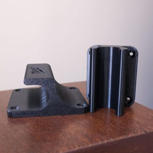 May include: Two black plastic wall mounts for a handrail. The mounts have a rectangular base with screw holes and a curved, open-ended top.